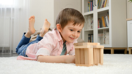 Smiling boy lying on floor and building house or tower from wooden blocks. Concept of child education and games at home © Kyrylo Ryzhov