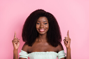 Portrait of attractive cheerful wavy-haired girl demonstrating up copy empty space ad isolated over pink pastel color background