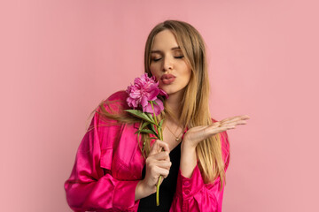 Close up  photo of pretty blond woman posing with pion flower in  stylish summer outfit over pink background.