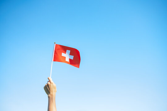 hand holding Switzerland flag on blue sky background. Switzerland National Day and happy celebration concepts