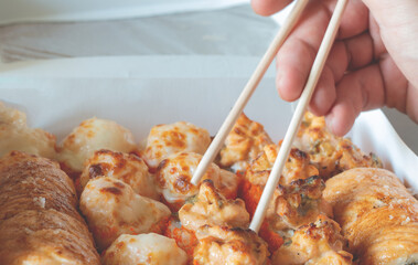 hand holding roll with chopsticks. Lunch boxes, sushi set. Assorted rolls on light background. Restaurant delivery, takeaway concept. Japanese cuisine seafood