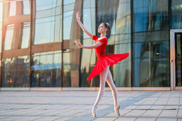 young ballerina in a red tutu is dancing against backdrop of cityscape