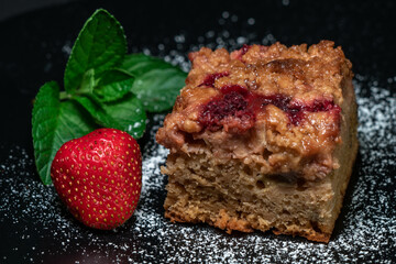 Closeup shot of a freshly baked cake with raspberries, jostaberries and rhubarb on a black plate isolated on black background with mint leaves and strawberry.