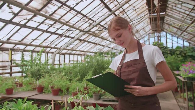 The woman works in the greenhouse and checks the presence of the right flowers on the customer's list