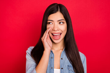 Photo of young attractive asian girl happy positive smile tell gossip news advert yell look empty space isolated over red color background