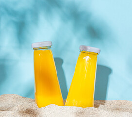 Two bottles with orange juice on the beach in the shade of tree leaves