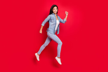 Fototapeta na wymiar Photo portrait girl in jeans outfit jumping up running fast isolated on bright red color background