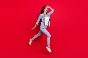 Photo portrait girl cheerful overjoyed in jeans clothes jumping up running fast looking far isolated on bright red color background