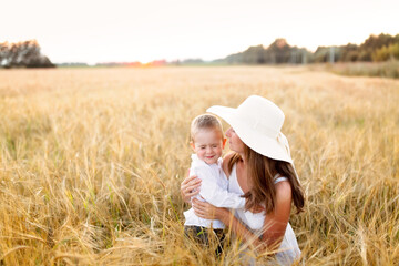 Motherhood. Toddler toddler boy with mom in a field at sunset in summer, beautiful summer photo, blur and soft focus, very warm photo, toning