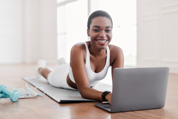 Young black woman lying on yoga mat using laptop