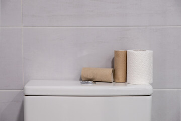 White toilet with some finished rolls of paper and others without touching.