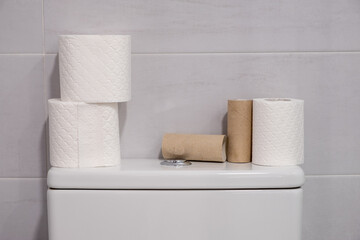 White toilet with some finished rolls of paper and others without touching.