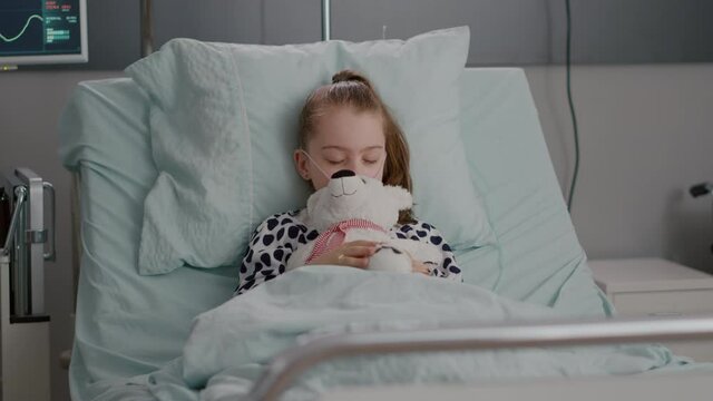 Portrait of tired sick child sleeping after suffering medical recovery surgery during disease examination in hospital ward. Hospitalized kid resting in bed wearing oxygen nasal tube