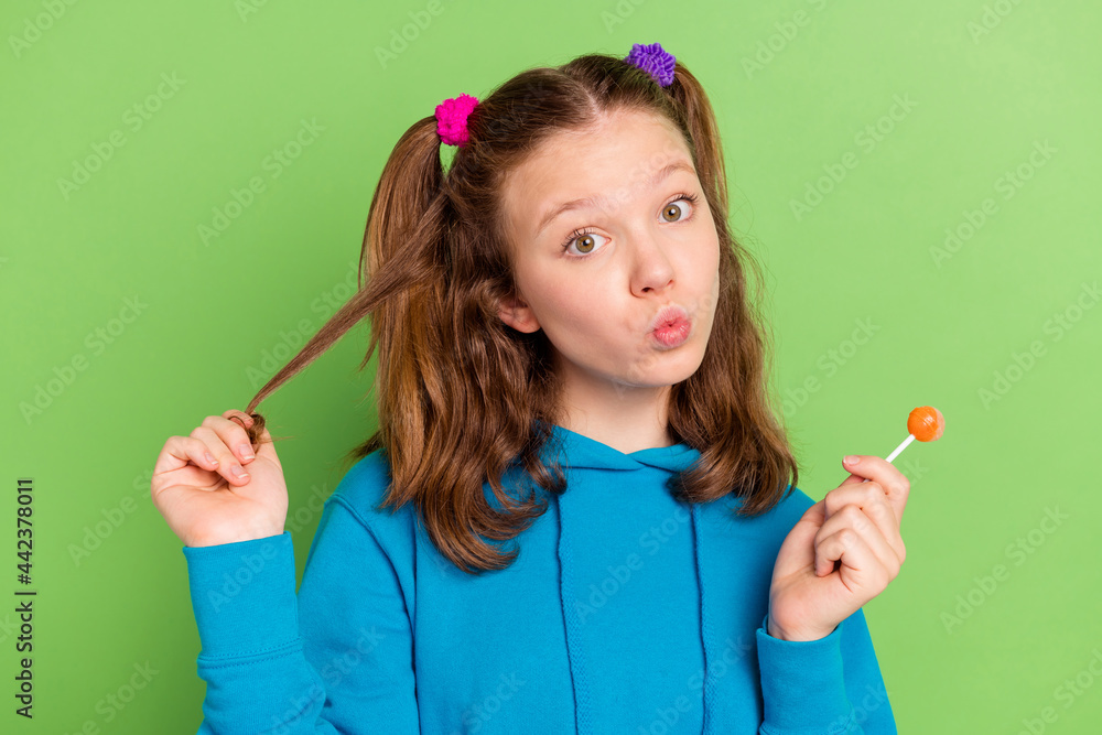 Poster Photo of cheerful young funky happy little girl hold hand lollipop good mood isolated on green color background