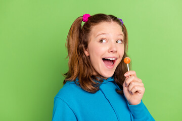 Photo of cheerful happy positive teenage girl look empty space hold candy isolated on green color...