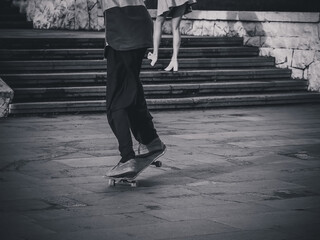 The guy rides a skateboard preparing for a stunt against the background of a girl climbing the stairs in a miniskirt. Black and white photo