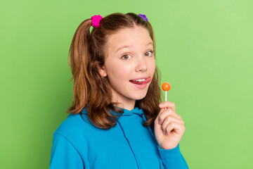 Photo of cheerful young little happy girl lick lips hold tasty candy good mood isolated on green color background - obrazy, fototapety, plakaty