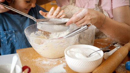 Smiling boy with young mother making dough in kitchen