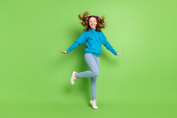 Full size photo of cheerful young happy small girl fly wind hair smile sportive isolated on green color background