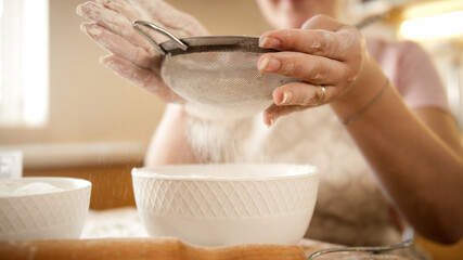 Sifting flour with metal sieve on domestic kitchen