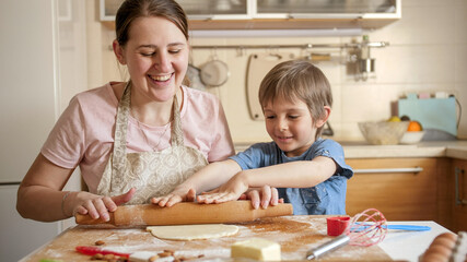 Happy smiling mother with son rolling dough for pizza on kitchen