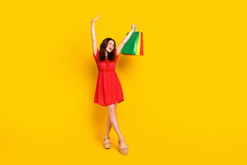 Full length portrait of positive girl closed eyes raise hands bags beaming smile isolated on yellow color background