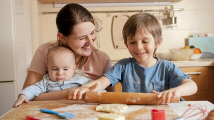 Happy family with kids rolling dough for biscuits or pie on kitchen. Children cooking with parents, little chef, family having time together, domestic kitchen.
