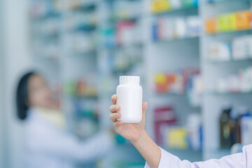 Close up white medicine bottle on holding hand and female pharmacist in pharmacy background