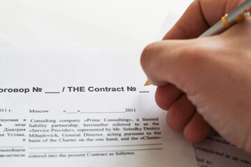 A businessman sitting at an office desk signs a contract with a shallow emphasis on signing....