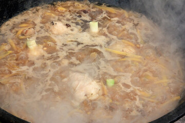 Zirvak for pilaf, meat, lamb fat, yellow carrots, chickpeas, garlic and spices are fried in a large black cauldron with bubbles and steam, cooking food
