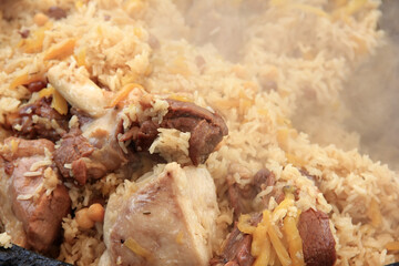 Delicious uzbek pilaf close-up with pieces of cooked lamb meat and lamb fat, rice, yellow carrots, cooking food