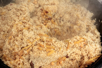 Freshly prepared delicious uzbek pilaf close-up, rice, yellow carrots, chickpeas, spices, cooking, steam is coming
