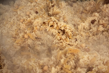 Freshly prepared delicious uzbek pilaf close-up, rice, yellow carrots, chickpeas, spices, cooking, steam is coming