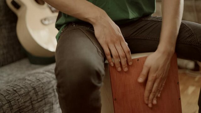 Crop musician playing cajon at home
