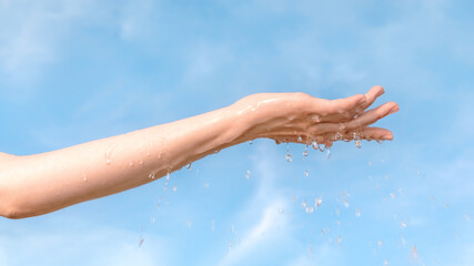 Woman hand with pure water drops against blue sky