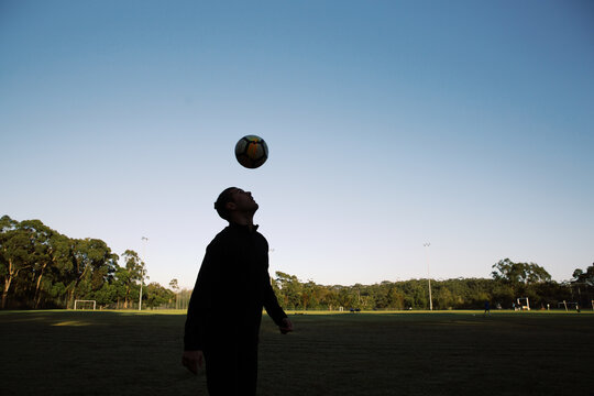 Silhouette shot of a man, head bouncing a ball soccer ball in the field with blue skies