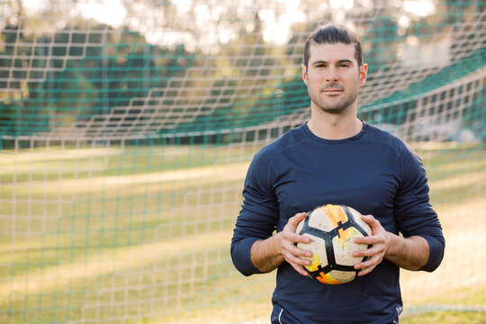 Fototapeta Close up shot of a man standing on the soccer filed, holding a soccer ball with a net behind