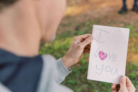 A letter with an I love you text and a red heart written on a small paper held by a man in blur