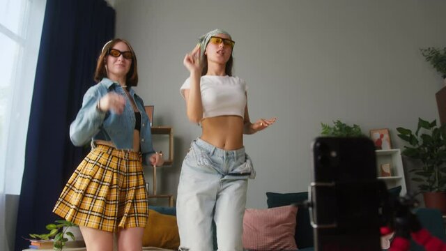 Young women recording dance trend video on modern smartphone camera in living room. Female students or teenagers dancing for musical clip. Bloggers making music content for channel.