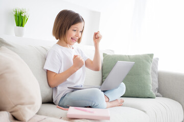 Photo portrait little girl sitting on couch talking on web camera passes test gesturing like winner