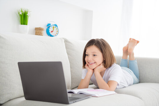 Photo portrait little girl laying on couch watch online lesson remote aducation at home