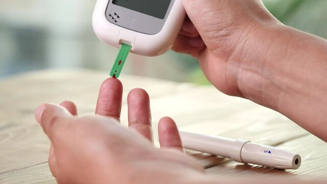 Close up diabetic test using lancet pen ad glucometer on finger with blood drop checking sugar level. Concept of World Diabetes Day, Glycemia, Hyperglycemia, Insulin, Healthcare and Medical.