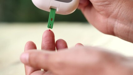 Close up diabetic test using lancet pen ad glucometer on finger with blood drop checking sugar level. Concept of World Diabetes Day, Glycemia, Hyperglycemia, Insulin, Healthcare and Medical.