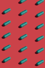 Vibrant colorful pattern of green medicine pill capsules on red background. Creative concept of overdose medicine usage and addiction to food supplement.