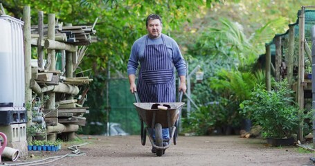 Caucasian male gardener walking with wheelbarrow at garden center - Powered by Adobe