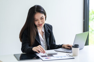 Beautiful Asian businesswoman holding a pen pointing to a graph Analyze presentation plan with laptop at the office.