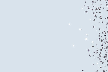 Metallic silver glittering stars confetti scattered on a blue pastel background with copyspace.