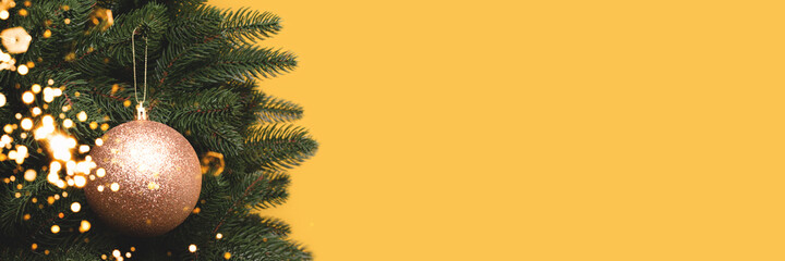 Banner with gold Christmas decoration. New Year bauble in front of yellow background with copyspace.