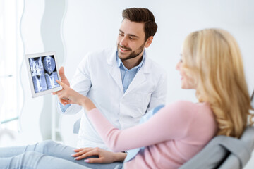 Fototapeta na wymiar Male dentist showing female patient x-ray on digital tablet