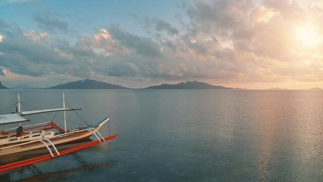 Philippines wooden boat in colorful sunset. Paradise background. Drone low fly over traditional Bangka ship. Pink clouds sky ferlect in calm sea water. Beautiful wild landscape. Exotic summer vacation